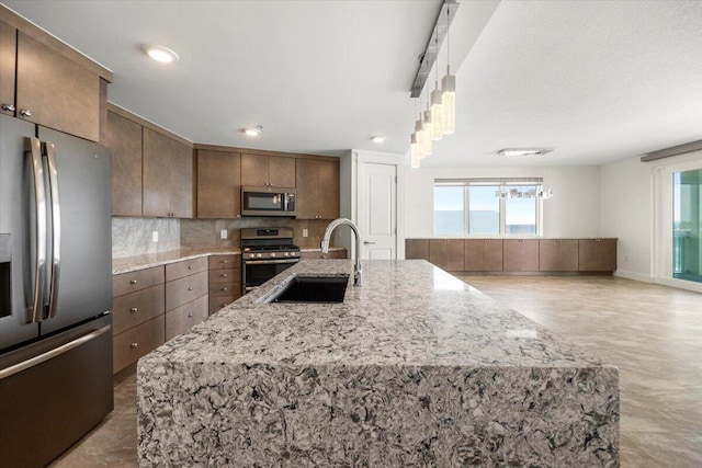 kitchen featuring appliances with stainless steel finishes, a sink, a center island with sink, and tasteful backsplash