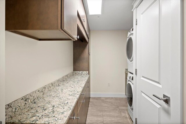 laundry area with light tile patterned floors, stacked washer and dryer, cabinet space, and baseboards