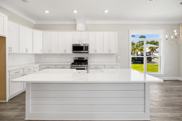 kitchen with appliances with stainless steel finishes, white cabinetry, light stone countertops, wood-type flooring, and crown molding