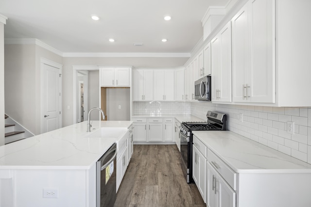 kitchen featuring an island with sink, sink, light stone countertops, white cabinets, and appliances with stainless steel finishes