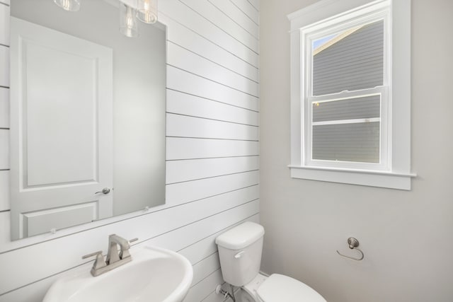 bathroom featuring sink, toilet, and wooden walls