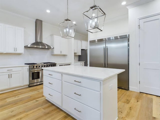 kitchen featuring high end appliances, wall chimney range hood, a center island, and white cabinets