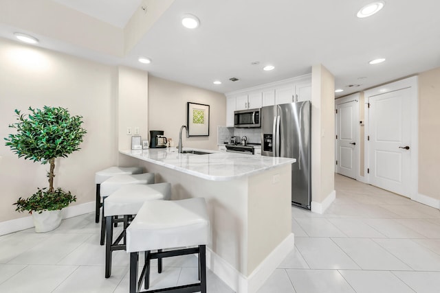 kitchen with appliances with stainless steel finishes, sink, kitchen peninsula, white cabinets, and a breakfast bar area