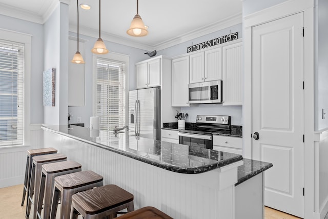 2452 Bungalo Ln, Miramar Beach, FL 32550 - kitchen with appliances with stainless steel finishes, a kitchen breakfast bar, wainscoting, white cabinets, and dark stone counters