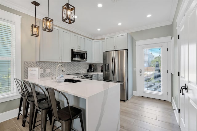 kitchen featuring light wood-type flooring, kitchen peninsula, a kitchen breakfast bar, stainless steel appliances, and pendant lighting