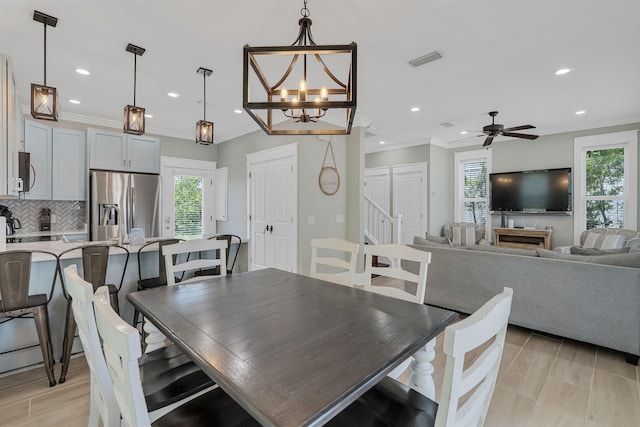 dining room with crown molding, light wood-type flooring, and ceiling fan with notable chandelier