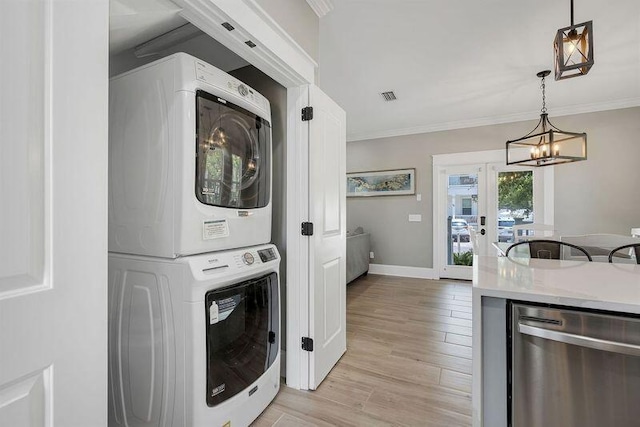 laundry room featuring stacked washing maching and dryer, crown molding, an inviting chandelier, and light wood-type flooring