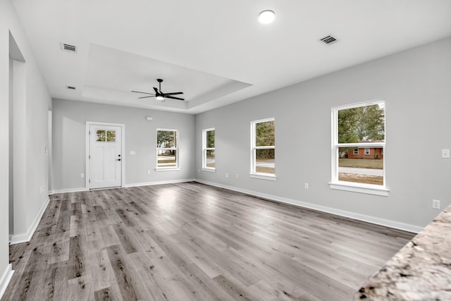 unfurnished living room featuring ceiling fan, light hardwood / wood-style floors, and a raised ceiling