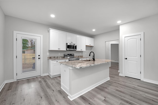 kitchen with appliances with stainless steel finishes, light stone counters, a kitchen island with sink, sink, and white cabinets