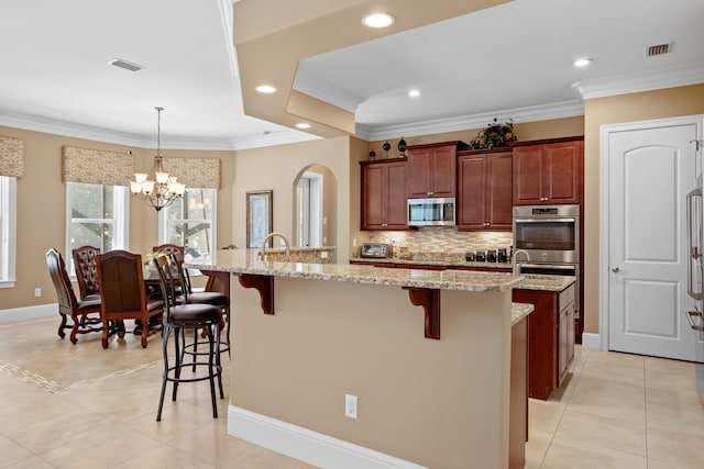 kitchen with a center island with sink, light tile patterned floors, appliances with stainless steel finishes, a breakfast bar, and light stone counters