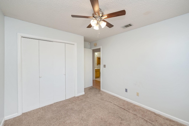 unfurnished bedroom featuring ceiling fan, a textured ceiling, light carpet, and a closet