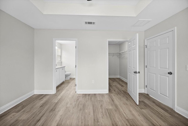 unfurnished bedroom with connected bathroom, light hardwood / wood-style floors, a closet, and a walk in closet