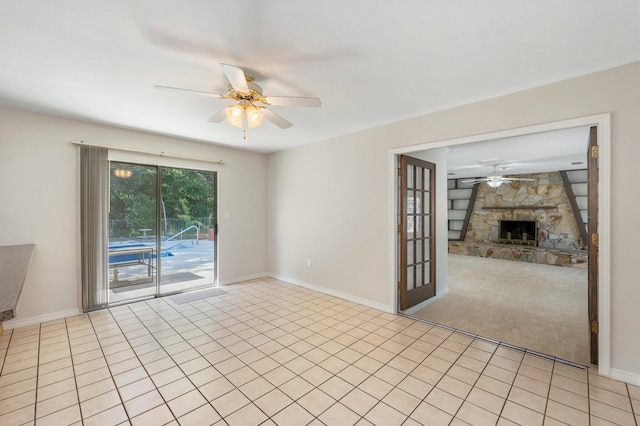 empty room featuring ceiling fan, a stone fireplace, and light tile patterned floors