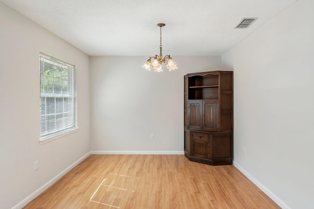 spare room featuring light hardwood / wood-style flooring, a textured ceiling, and an inviting chandelier