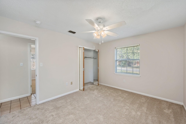 unfurnished bedroom featuring a closet, ceiling fan, light carpet, and a textured ceiling