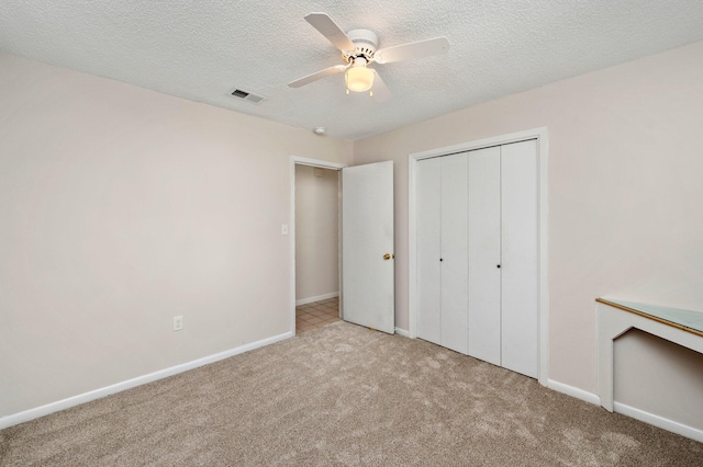 unfurnished bedroom featuring light carpet, a closet, a textured ceiling, and ceiling fan