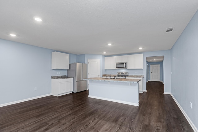 kitchen with dark wood-type flooring, light stone counters, white cabinets, a kitchen island with sink, and appliances with stainless steel finishes