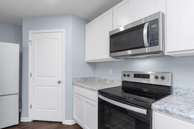 kitchen with white cabinets, dark hardwood / wood-style flooring, light stone counters, and appliances with stainless steel finishes