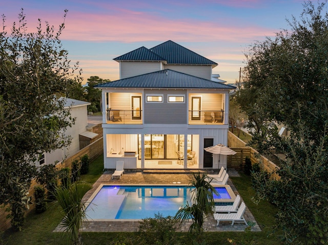 back house at dusk featuring a patio and a balcony