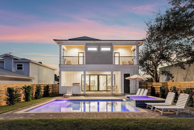 back house at dusk featuring a patio area, a balcony, and a fenced in pool