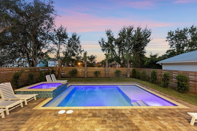 pool at dusk featuring a patio and an in ground hot tub