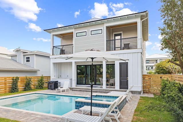 rear view of property featuring a pool with hot tub, a balcony, and a patio area