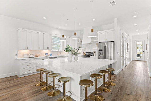 kitchen featuring hardwood / wood-style flooring, a breakfast bar, decorative light fixtures, a center island, and white cabinets