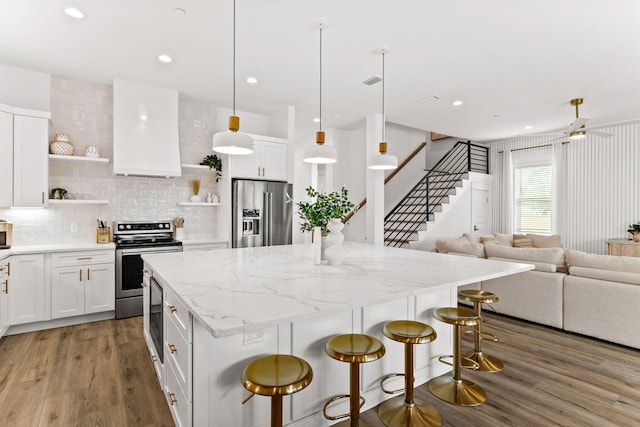 kitchen featuring stainless steel appliances, extractor fan, decorative light fixtures, white cabinets, and a center island