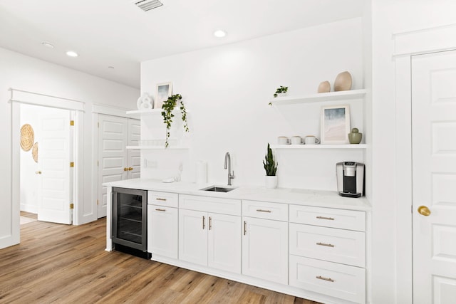 kitchen with sink, light stone countertops, white cabinetry, light wood-type flooring, and wine cooler