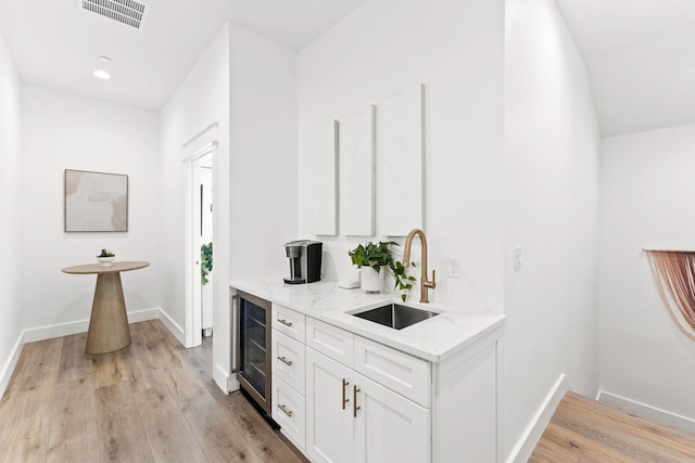 bar featuring light hardwood / wood-style floors, sink, light stone counters, and wine cooler