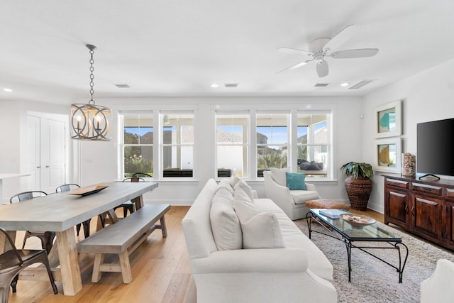 living room featuring ceiling fan with notable chandelier and light wood-type flooring