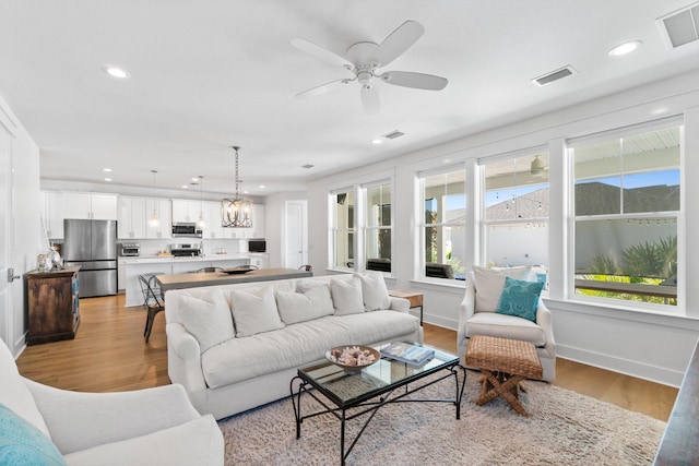 living room with light hardwood / wood-style floors and ceiling fan with notable chandelier