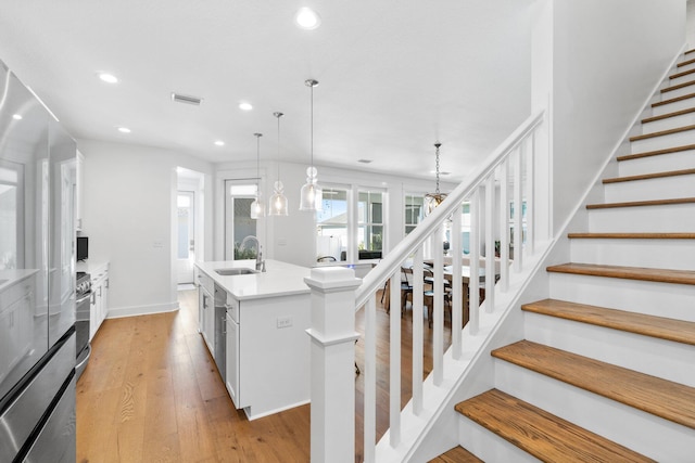 kitchen with sink, decorative light fixtures, light hardwood / wood-style flooring, white cabinetry, and an island with sink