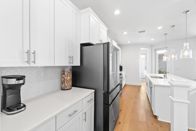 kitchen with stainless steel refrigerator, sink, hanging light fixtures, light hardwood / wood-style flooring, and white cabinets