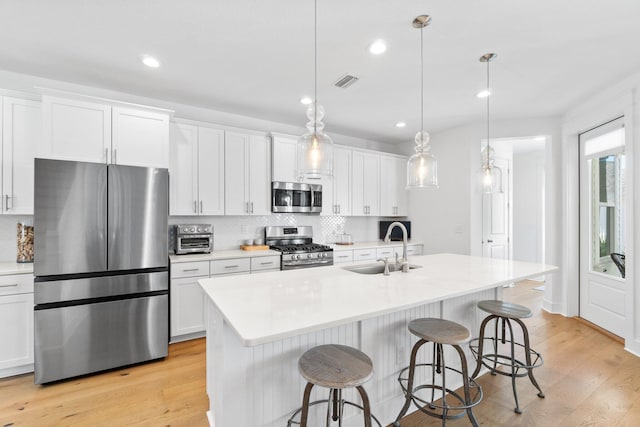 kitchen featuring sink, pendant lighting, a center island with sink, white cabinets, and appliances with stainless steel finishes