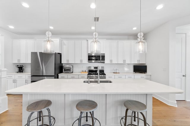 kitchen with pendant lighting, backsplash, a large island with sink, sink, and appliances with stainless steel finishes