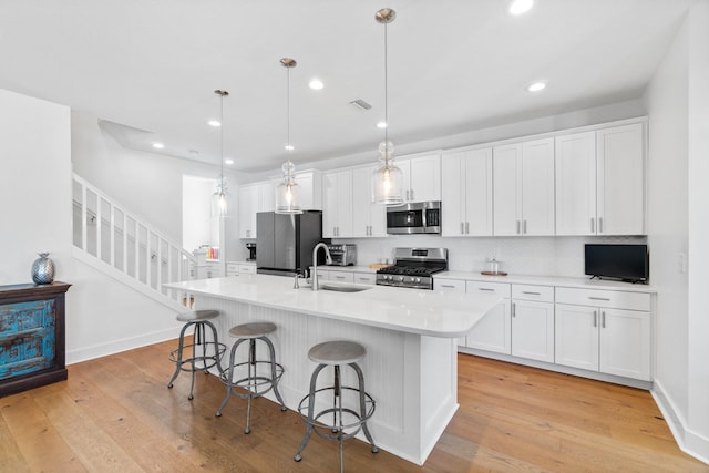 kitchen featuring sink, stainless steel appliances, pendant lighting, a kitchen island with sink, and white cabinets