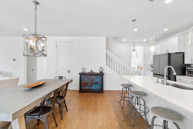 kitchen featuring white cabinets, sink, hanging light fixtures, a kitchen bar, and stainless steel refrigerator