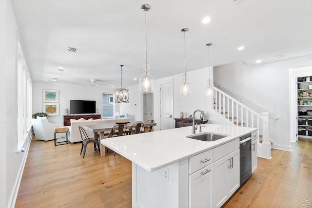 kitchen featuring pendant lighting, dishwasher, white cabinets, sink, and an island with sink