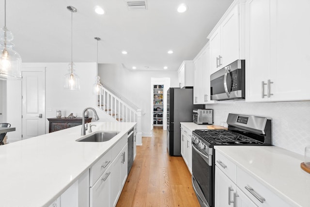 kitchen with appliances with stainless steel finishes, sink, pendant lighting, light hardwood / wood-style flooring, and white cabinetry