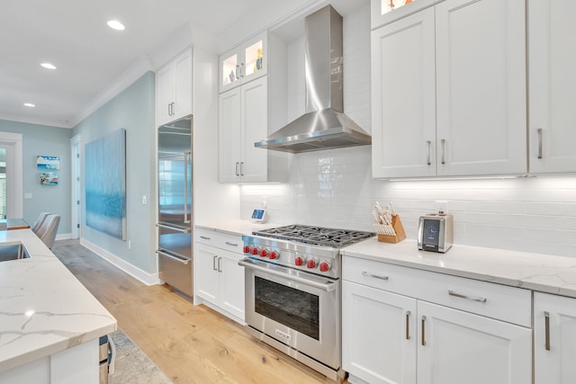 kitchen featuring light stone countertops, wall chimney range hood, light wood-type flooring, white cabinets, and high end appliances