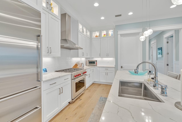 kitchen with wall chimney exhaust hood, high end appliances, sink, pendant lighting, and white cabinets