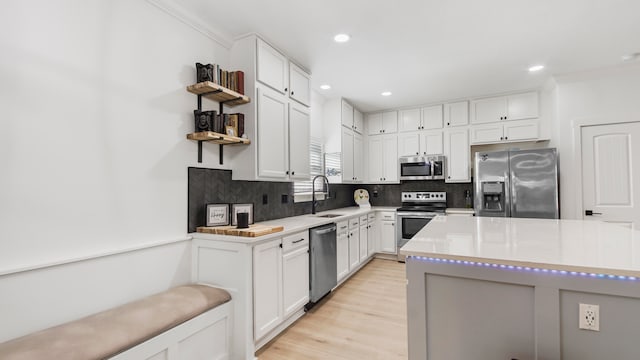 kitchen with crown molding, appliances with stainless steel finishes, sink, white cabinets, and light hardwood / wood-style flooring