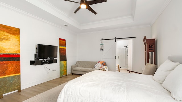 bedroom with a barn door, ceiling fan, crown molding, a tray ceiling, and light wood-type flooring