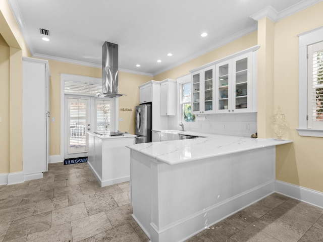 kitchen with kitchen peninsula, plenty of natural light, stainless steel fridge, white cabinets, and exhaust hood