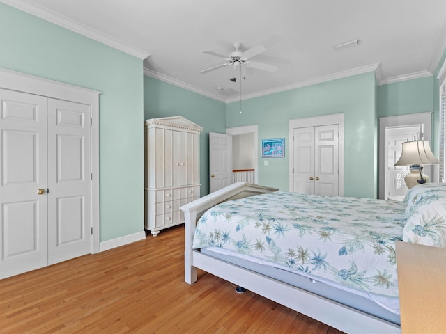 bedroom featuring ornamental molding, two closets, wood-type flooring, and ceiling fan