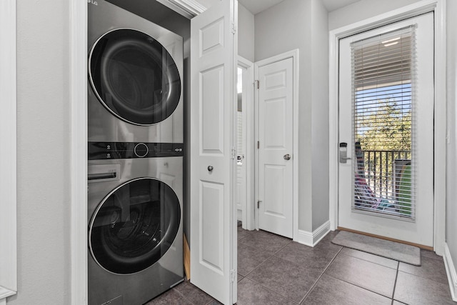 clothes washing area featuring stacked washer and dryer, dark tile patterned floors, laundry area, and baseboards