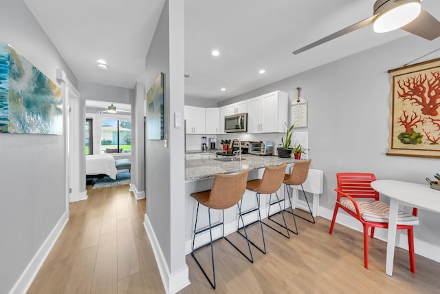 kitchen featuring white cabinetry, light stone counters, kitchen peninsula, a breakfast bar area, and light wood-type flooring