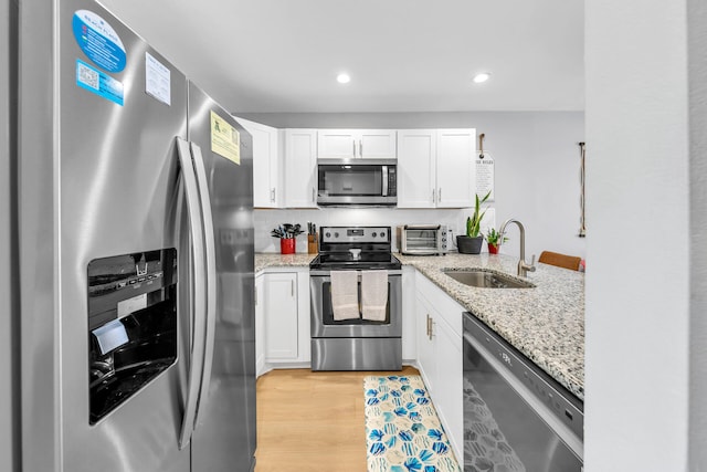 kitchen with white cabinetry, sink, light stone countertops, light hardwood / wood-style flooring, and appliances with stainless steel finishes