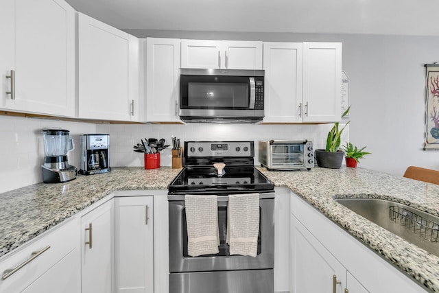 kitchen featuring backsplash, light stone countertops, white cabinets, and stainless steel appliances